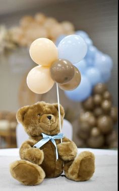 a brown teddy bear sitting on top of a table with balloons in the shape of flowers