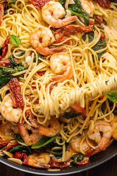 pasta with shrimp, spinach and sun dried tomatoes in a skillet on a wooden table