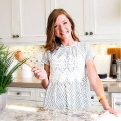 a woman standing in a kitchen holding a wooden spoon