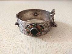 A pretty Moroccan silver bracelet, hinged and closed with a pin mechanism. On either side are enamel plaques at the center of which sits a faceted red glass cabochon. Inner diameter : 5,6 cm (2,2 inches) Width : 2,4 cm (0,9 inches) Weight : 55 g Enamel Bracelet Jewelry For Wedding, Collectible Enamel Bangle Jewelry, Ornate Enamel Jewelry For Ceremonial Use, Ornate Enamel Jewelry For Ceremonial Occasion, Ornate Ceremonial Enamel Jewelry, Collectible Enamel Bracelet Jewelry, Antique Silver Cabochon Bracelets, Ornate Hinged Bracelets For Gifts, Ornate Silver Enamel Jewelry