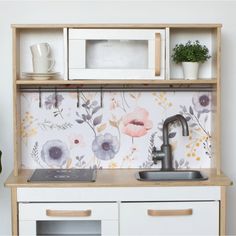 a kitchen with floral wallpaper and white cabinets