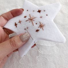 a hand holding a star ornament made out of white felt with gold stars on it