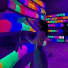 a woman standing in front of a wall with colorful lights on it and she is painting the walls