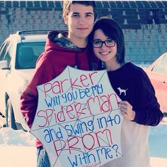 a young man and woman standing next to each other in the snow holding a sign