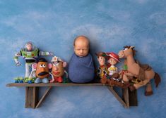 a baby laying on top of a wooden shelf with toy characters around him and behind it