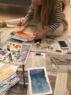 a woman is sitting on the floor working on some art work with watercolors