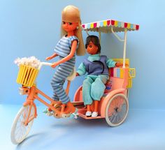 two dolls riding on the back of a toy bike