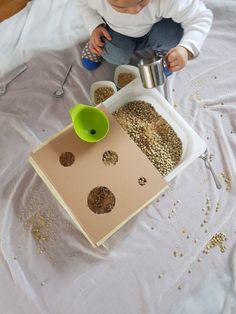 a baby sitting on top of a bed next to a container filled with grains and a measuring cup