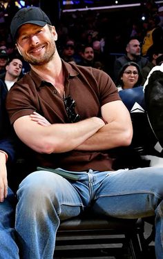 a man with his arms crossed sitting on a bench in front of an audience at a basketball game