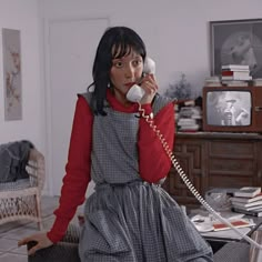 a woman is talking on the phone while sitting in a living room with an old fashioned telephone