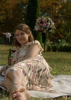 a woman sitting on top of a blanket next to a bottle of wine in the grass