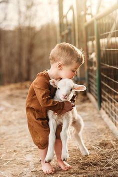 a little boy holding a baby goat in his arms