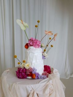 a wedding cake decorated with flowers on a white tableclothed cloth draped around it