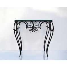 an iron and glass console table with intricate designs on the top, sitting against a white wall