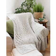 a white blanket sitting on top of a couch next to a potted plant