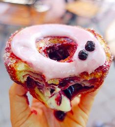 a person is holding up a doughnut with berries on it and frosted in icing