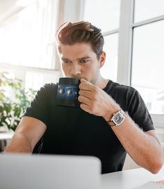 a man holding a coffee cup in front of his face while looking at a laptop