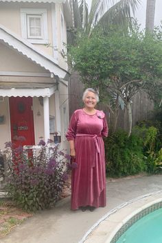 an older woman standing in front of a house next to a swimming pool and palm trees