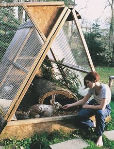 a woman kneeling down next to a rabbit in a coop