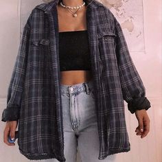 a woman standing in front of a white wall wearing jeans and a black crop top