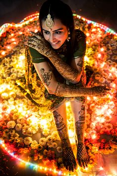 a woman sitting on top of a flower covered ground with lots of lights around her