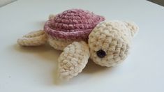 a small stuffed turtle sitting on top of a white table next to a red and pink hat