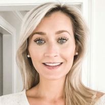 a woman with blonde hair and blue eyes smiling at the camera while standing in front of a door