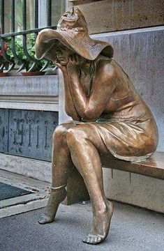 a bronze statue of a woman sitting on a bench with her head in her hands