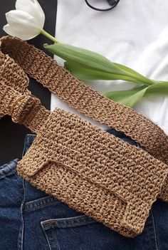 a crocheted tie laying on top of a pair of jeans next to a white tulip