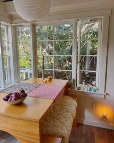 a dining room table with fruit on it in front of two windows and candles lit