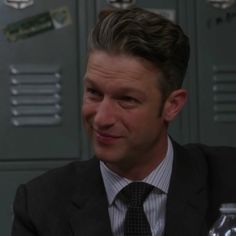 a man wearing a suit and tie sitting in front of lockers with water bottles