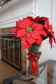 a vase filled with red poinsettias on top of a table next to a fireplace