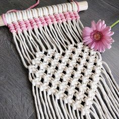 a pink flower sitting on top of a table next to a piece of white yarn