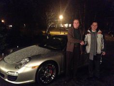 two people standing next to a silver sports car