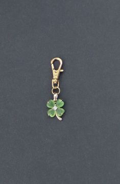 a green clover charm hanging from a gold plated key chain on a black surface