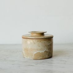 a ceramic jar with a lid sitting on a marble countertop next to a white wall