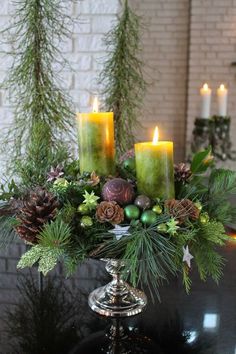 candles are lit on top of a table with evergreen and pineconis in the center