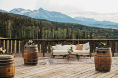 a wooden deck with two couches and three wine barrels on it, overlooking the mountains