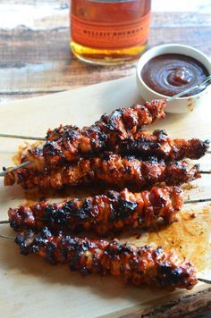 several skewers of meat sitting on top of a cutting board next to a bottle of ketchup