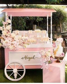 a pink and white dessert cart with cupcakes on the top is decorated with flowers