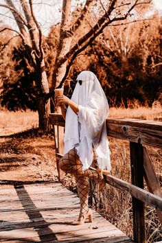 a woman dressed in white is standing on a wooden bridge