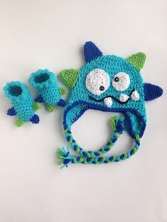 a crocheted blue hat with green ears and eyes on top of a white surface