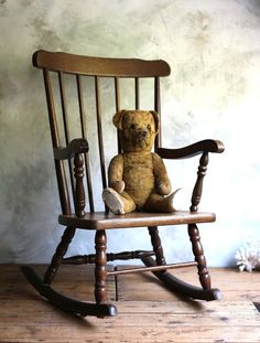 a brown teddy bear sitting in a wooden rocking chair on a wood floor next to a wall