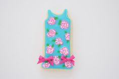 a cookie shaped like a tank top with pink flowers on it and a bow around the neck