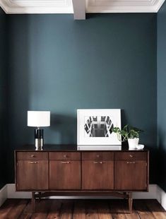 a living room with blue walls and wooden furniture in the corner, along with a white framed photograph on top of an old dresser