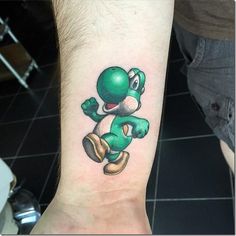 a green cartoon character tattoo on the left wrist and foot, with an arm band