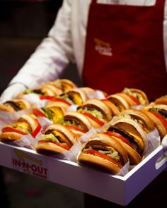 a man holding a tray full of hotdogs with condiments on them