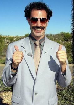 a man in a suit and tie giving the thumbs up sign with sunglasses on his head