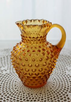 a yellow glass vase sitting on top of a white doily covered tablecloth with holes in it