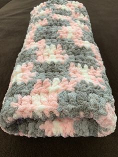 a crocheted blanket laying on top of a black bed covered in pink and gray